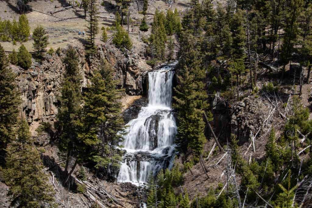 A couple of hikers walk past Undine Falls on the Lava Creek Trail, one of the best spring hikes in Yellowstone National Park