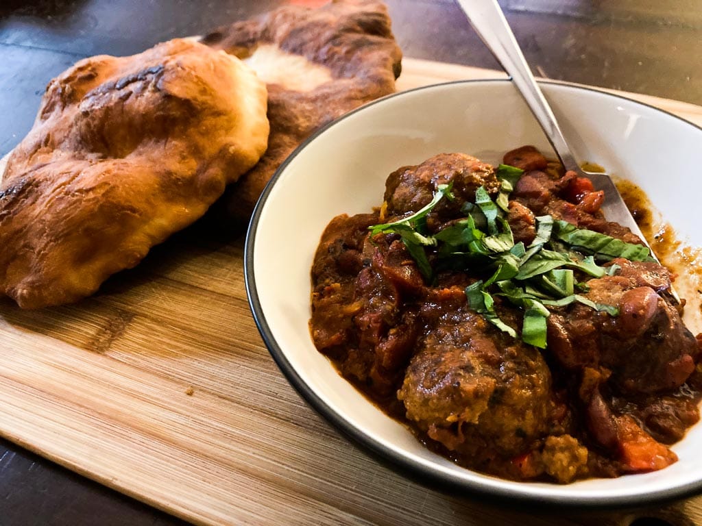 Bison meatballs in smoky pepper tomato beans sauce with fry bread on cutting board