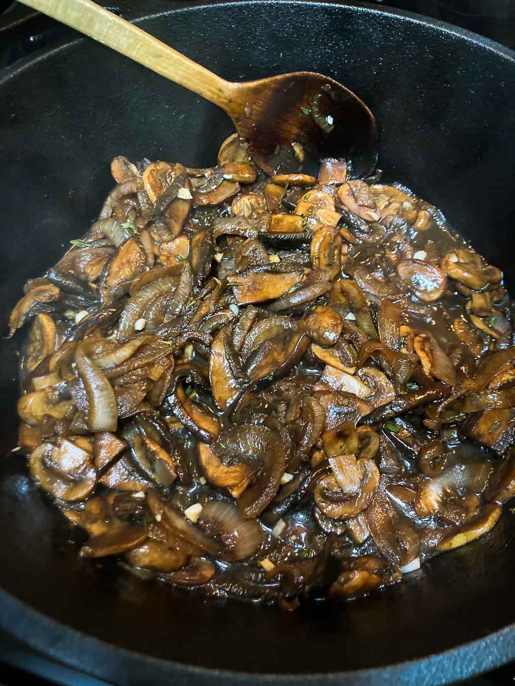 Mushrooms braising in cast-iron pot on stove with balsamic and onions