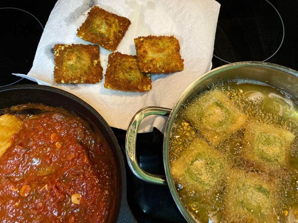 Raviolis toasting in pot with marinara sauce on the side