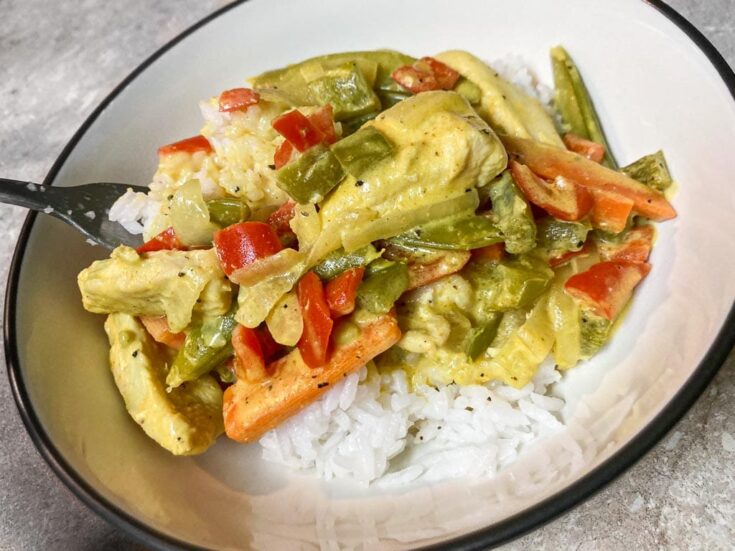 Creamy curried chicken over white rice in bowl with fork